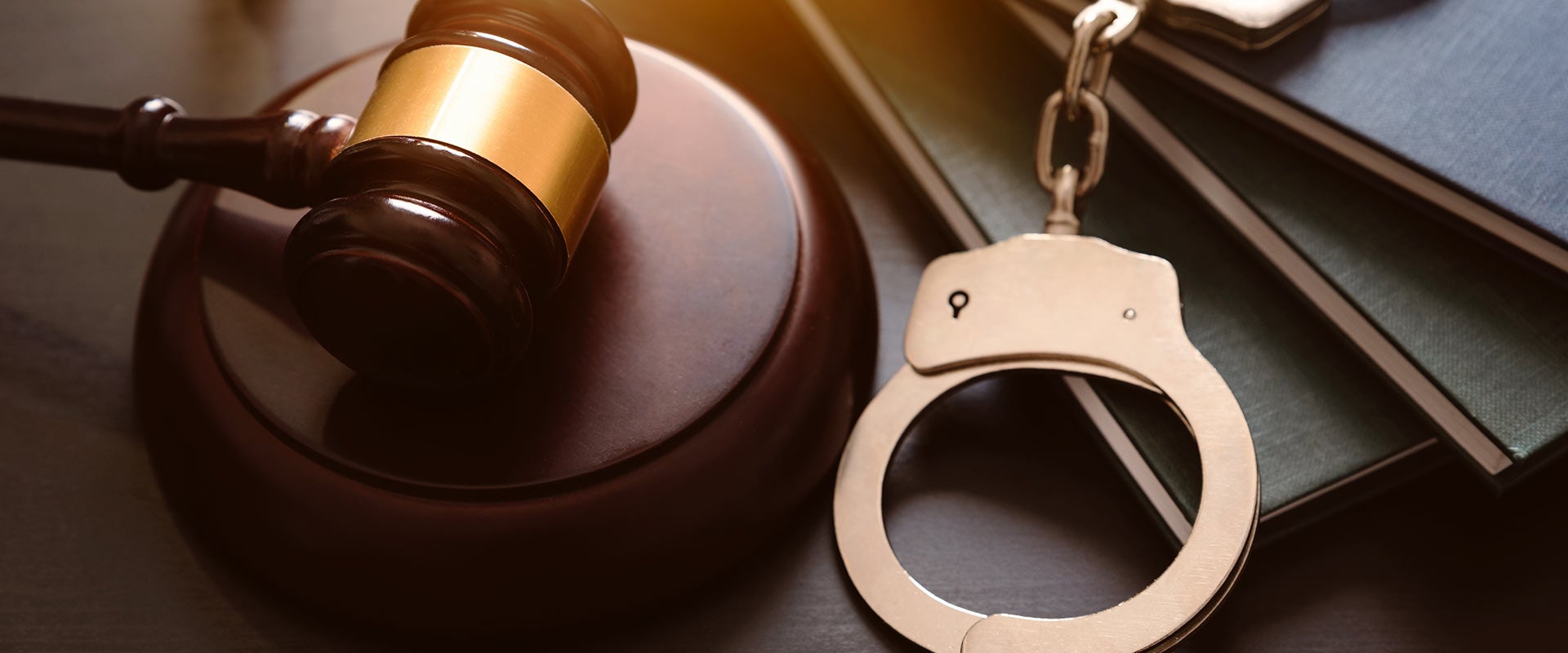 A wooden gavel next to metal handcuffs, all resting on dark books.