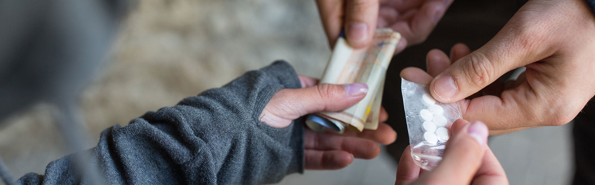 Two hands exchanging money and pills in a plastic bag, showing drug transaction.
